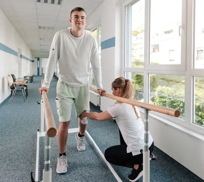 A specialist working with an individual who is in rehab and relearning how to walk. 