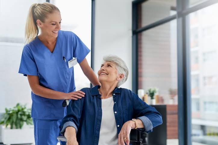 nurse talking to elderly woman patient in wheelchair who is smiling 