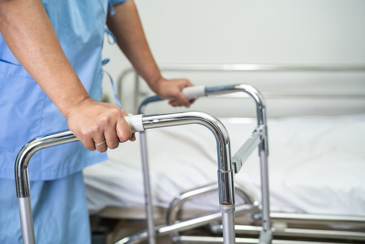 A woman walking with a walker while still in the hospital awaiting post-hospital care. 