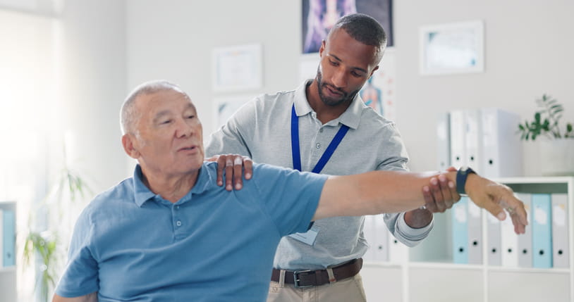 A physical therapist is working on an elderly man's arm during a session. 