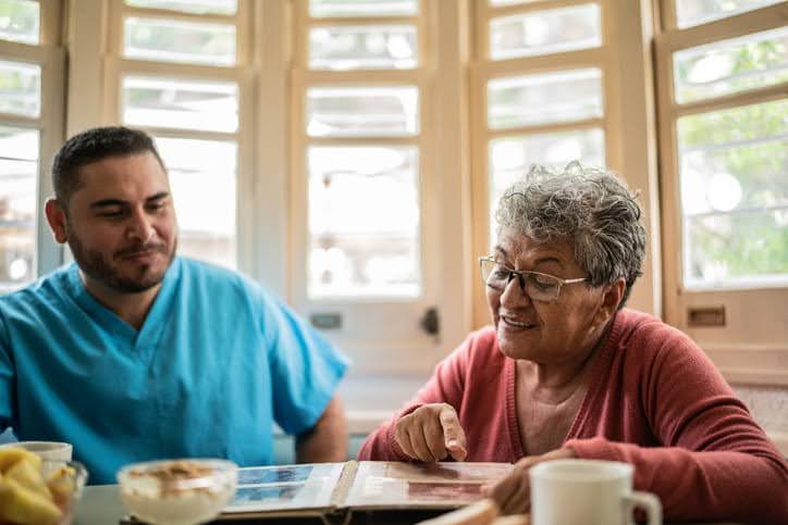 A male nurse looking at a photo album with an elderly woman in a skilled nursing facility 