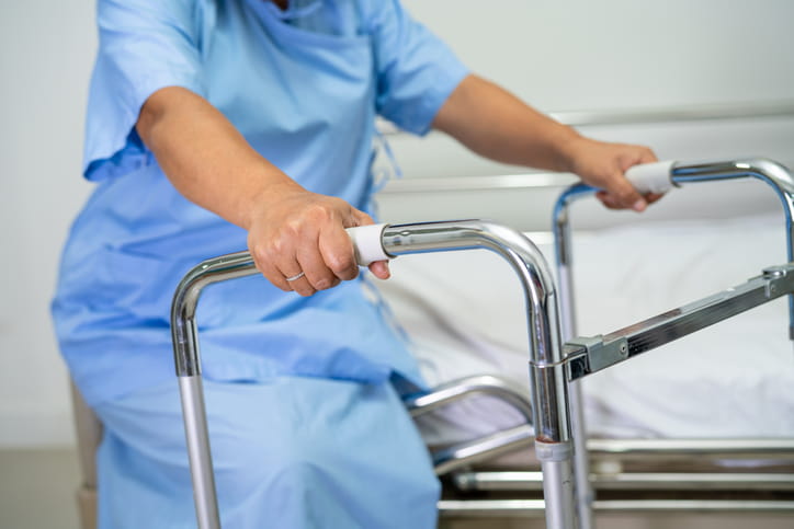 A woman in a hospital gown sitting with a walker. 