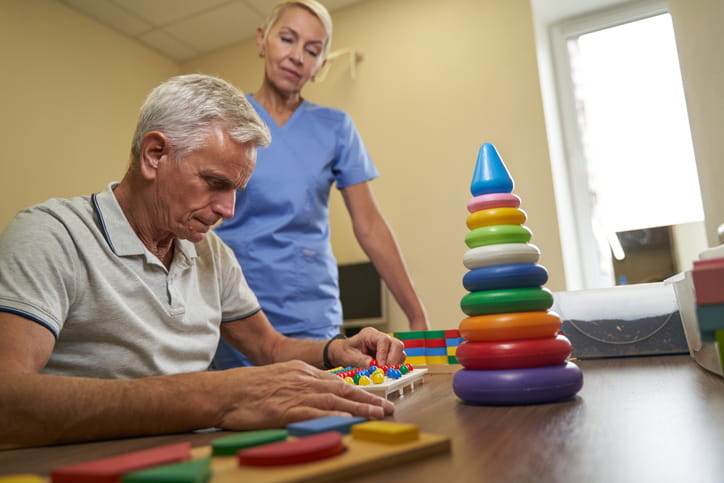 What Is The Difference Between Occupational Therapy And Physical Therapy? 1 An occupational therapist helps a patient with his exercise of stacking items.