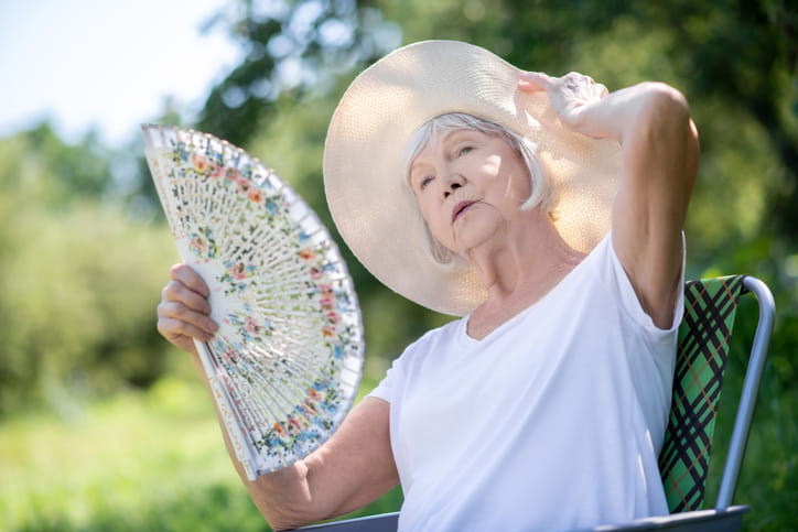 An older women fanning herself in the hot summer sun