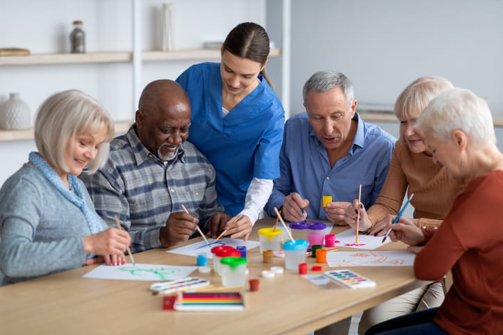 A nurse assisting seniors at a skilled nursing facility as they paint together.