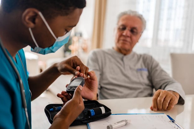 A skilled nursing care nurse checks the blood sugar level on a patient.