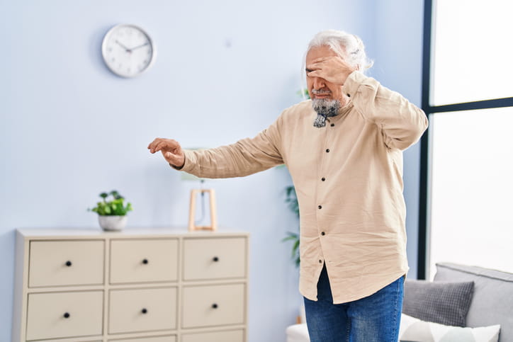 An elderly man holding his head as he stands due to vertigo.