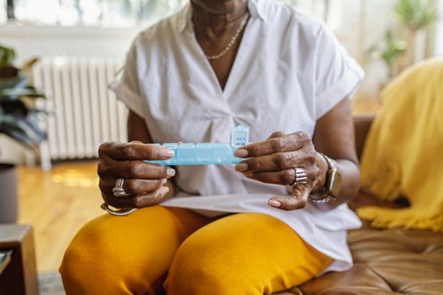 A senior holding a weekly medication tray.