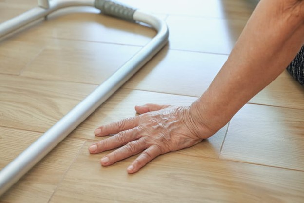 An elderly woman is next to her walker on the ground after a fall.
