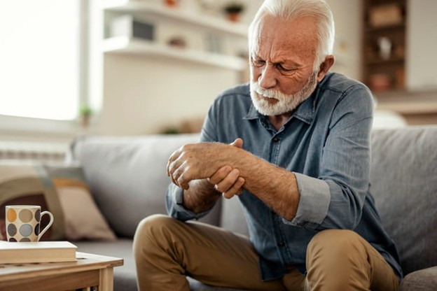 An elderly man holds his wrist due to arthritis.