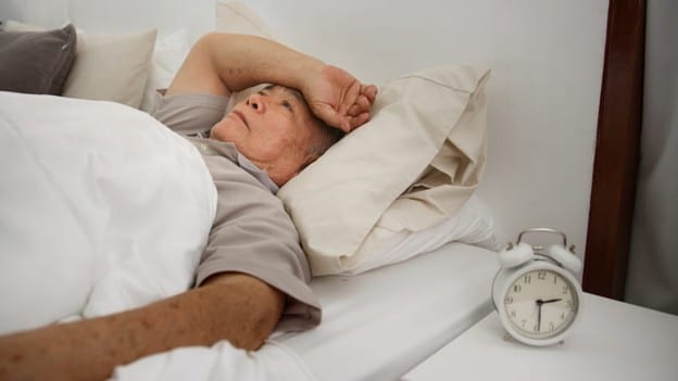 Excessive Sleepiness In Seniors 2 An elderly man appears distressed as he lays in bed.