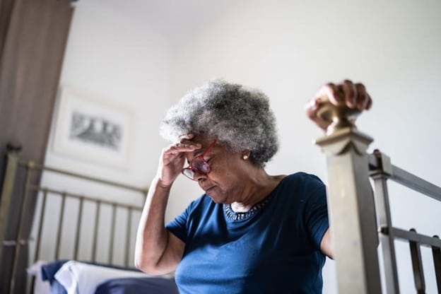 What Causes Dizziness In The Elderly? 2 An elderly woman sits on her bed, holding her head, due to dizziness.