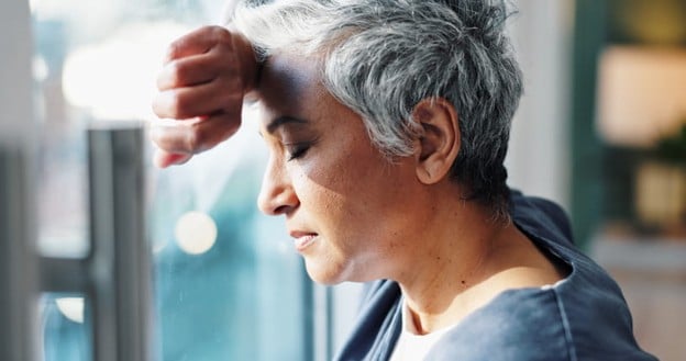 Caregiver Burnout: Signs, Symptoms, And When To Ask for Help 2 A woman leans her head against her arm on the window as she experiences caregiver burnout.