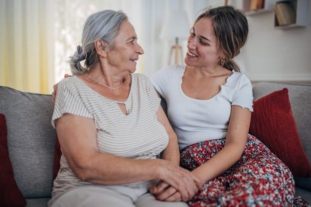 What Adult Children Should Know Before Becoming A Caregiver 2 A daughter sits and smiles with her elderly mother.